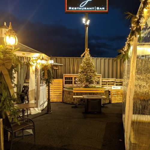 Outdoor dining area at night, featuring a Christmas tree, festive lights, and cozy seating arrangements.