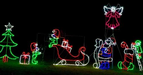 Colorful Christmas lights depicting Santa, an angel, a tree, and gifts in a festive scene against a dark background.