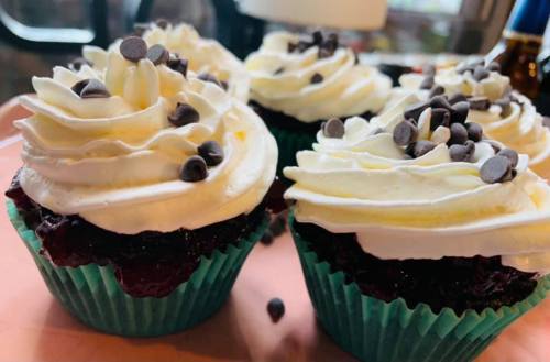 Close-up of chocolate cupcakes with white frosting and chocolate chips, placed on a pink tray.