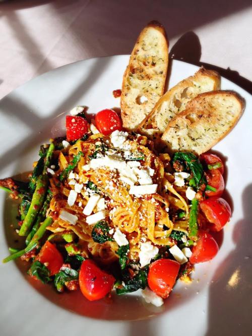 A plate of pasta with spinach, tomatoes, and feta, garnished with toasted bread slices.