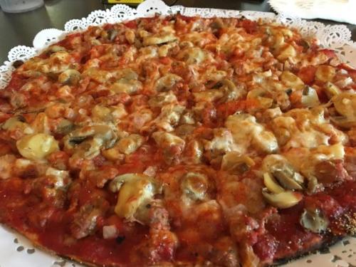 A close-up of a pizza topped with melted cheese, mushrooms, and ground meat on a decorative paper plate.