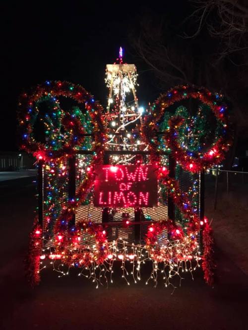 A festive float decorated with colorful lights and a sign reading "TOWN Limon," set against a night sky.