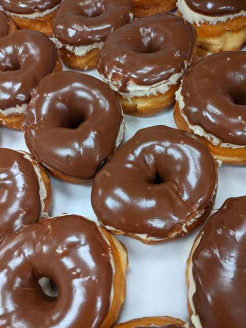 A close-up of freshly glazed chocolate donuts arranged closely together.