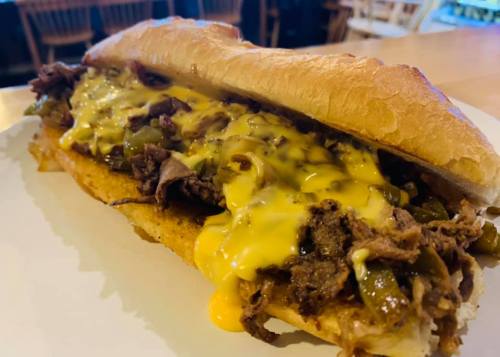 A loaded sandwich with tender beef, melted cheese, and green peppers on a toasted hoagie roll.