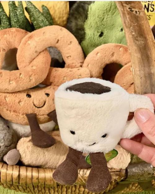 A cute plush coffee cup with legs, surrounded by other food-themed plush toys in a basket.