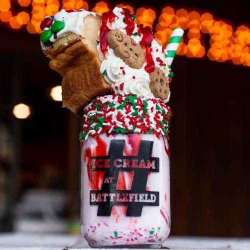 A colorful milkshake topped with whipped cream, cookies, and festive sprinkles in a jar with "Ice Cream at Battlefield" label.
