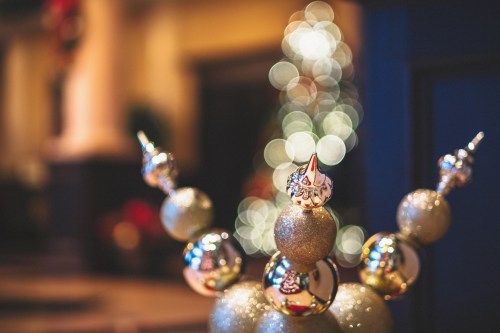 A close-up of decorative ornaments with a blurred Christmas tree in the background, creating a festive atmosphere.