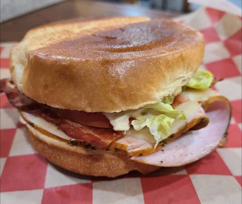 A sandwich with layers of lettuce, tomato, bacon, and turkey on a toasted bun, served on a checkered paper.
