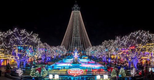 A festive winter scene at Kings Island, featuring a lit Christmas tree, ice skating rink, and colorful holiday lights.