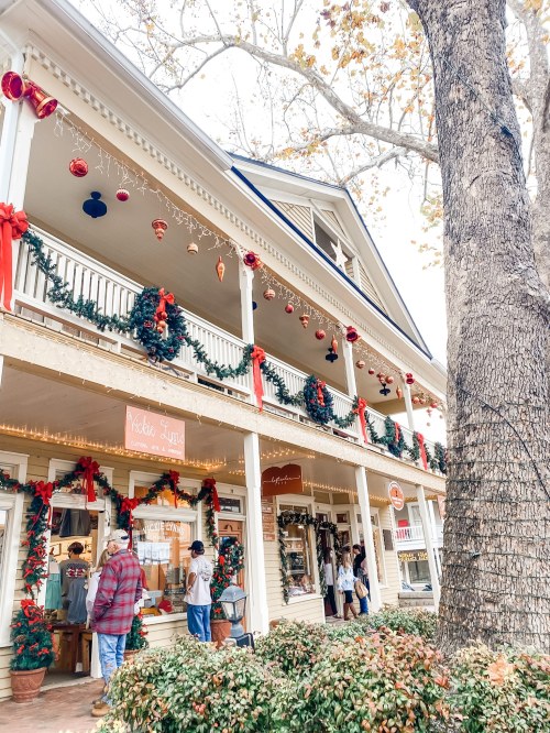 A festive storefront decorated with holiday garlands and ornaments, with people browsing outside.