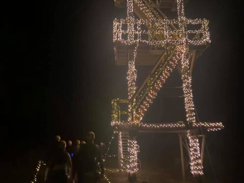 A group of people walks towards a tall structure adorned with bright lights at night.