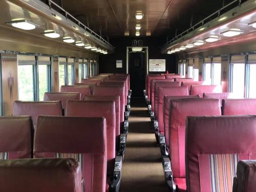 Interior of a vintage train car featuring rows of maroon seats and large windows, creating a spacious, nostalgic atmosphere.