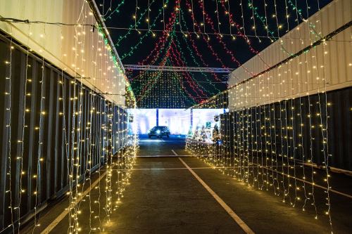 A pathway lined with colorful string lights, leading to a brightly lit area in the distance.