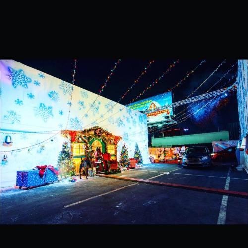 A festive outdoor scene with Christmas decorations, lights, and trees, set in a parking lot at night.