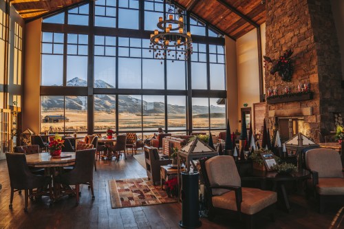 Cozy lodge interior with large windows showcasing mountain views, wooden beams, and festive decorations.