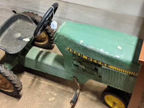 A vintage green toy tractor with a black seat and wheels, labeled "John Deere," displayed indoors.