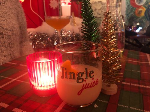 A festive table setting with a "Jingle Juice" drink, a red candle, and small Christmas trees in the background.