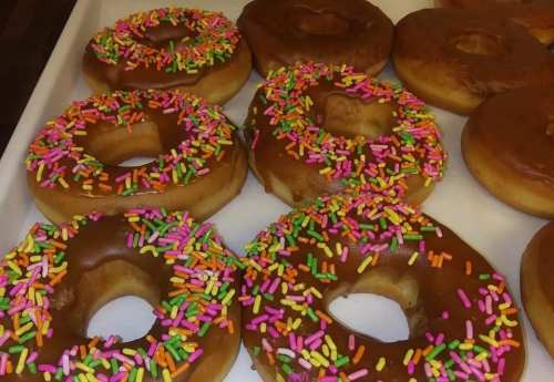 A tray of glazed donuts topped with colorful sprinkles in various arrangements.