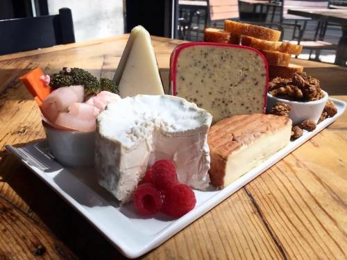 A cheese platter featuring various cheeses, shrimp, vegetables, raspberries, and toasted bread on a wooden table.