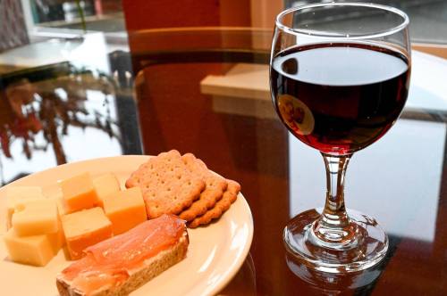 A plate of cheese cubes and crackers beside a glass of red wine on a table.