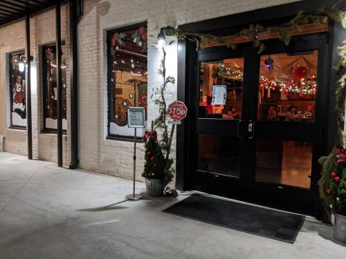 Entrance of a festive restaurant decorated with holiday lights and greenery, featuring a "STOP" sign.
