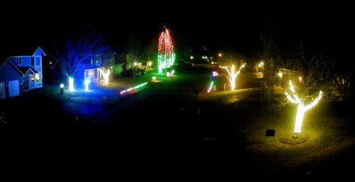 A nighttime scene of a neighborhood decorated with colorful holiday lights on houses and trees.