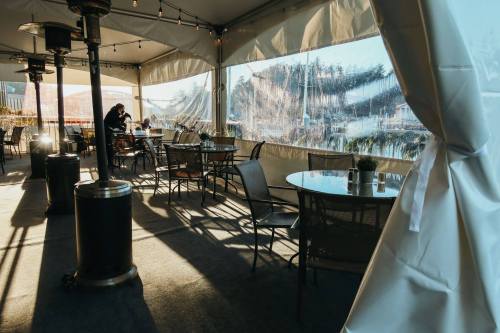A cozy outdoor dining area with tables and chairs, illuminated by sunlight, overlooking a scenic view.