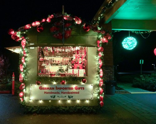 A festive gift stall adorned with Christmas lights and decorations, featuring a sign for "German Imported Gifts."