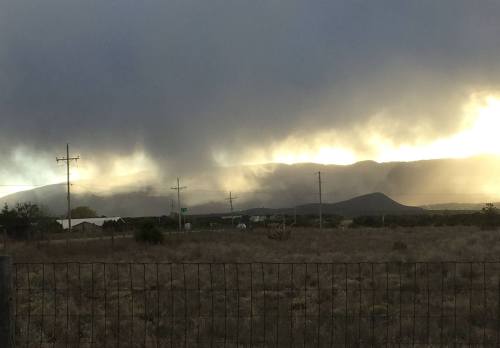 A cloudy sky over distant mountains, with power lines and a grassy field in the foreground.