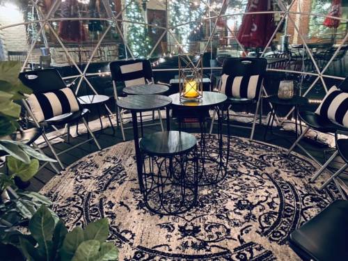 Cozy indoor seating area with black and white chairs, tables, and a decorative rug, surrounded by string lights.