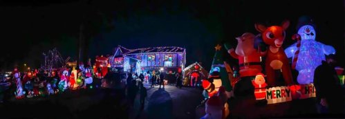 A festive house decorated with colorful Christmas lights and large inflatable characters, including Santa, Rudolph, and a snowman.