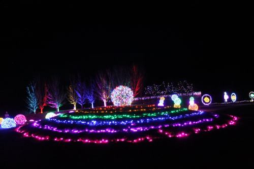 Colorful holiday lights illuminate a circular garden with trees and decorative snowmen against a dark night sky.