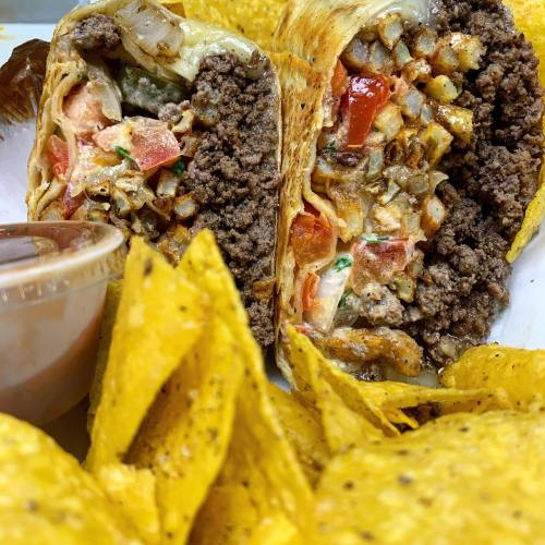 A close-up of a burrito filled with beef, vegetables, and cheese, served with tortilla chips and a side of sauce.