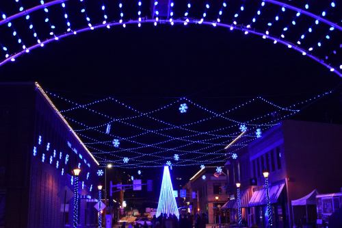 A festive street scene illuminated with blue lights and snowflake decorations, featuring a glowing Christmas tree.