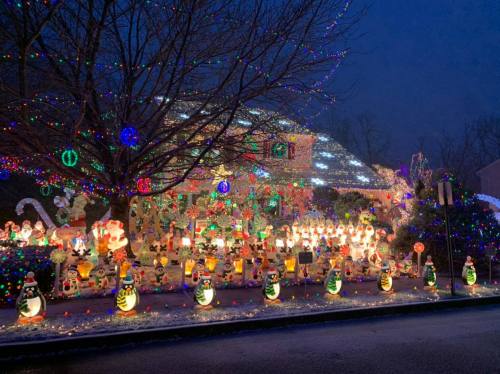 A festive house decorated with colorful lights and illuminated holiday figures, surrounded by snow at dusk.