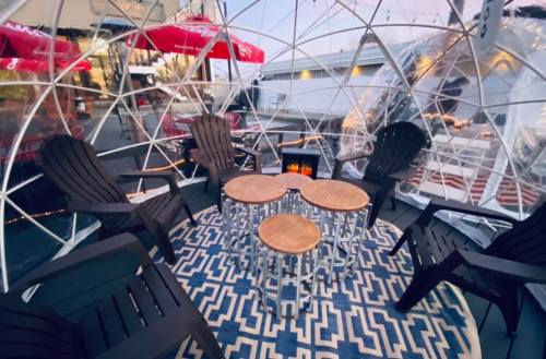 Cozy outdoor dining igloo with wooden tables, chairs, and a patterned rug, illuminated by soft lights.