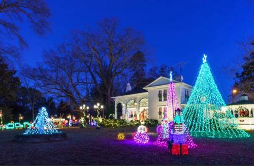 A beautifully decorated house with colorful Christmas lights and illuminated trees in a festive evening setting.