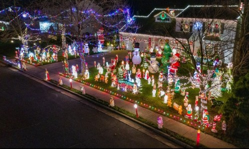 A festive yard decorated with numerous colorful Christmas lights and holiday figures, including snowmen and Santa Claus.