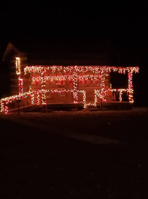 A log cabin decorated with colorful lights, glowing warmly against a dark night sky.