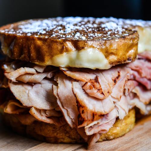 A close-up of a sandwich with layers of sliced ham between two pieces of golden, toasted bread.