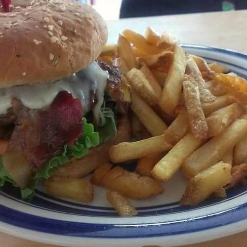 A sesame seed bun burger with bacon, lettuce, and mayo, served with a side of golden French fries on a plate.