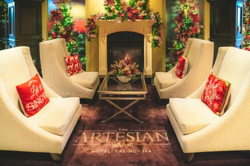 Cozy hotel lobby with festive decorations, plush chairs, and a fireplace, creating a warm, inviting atmosphere.