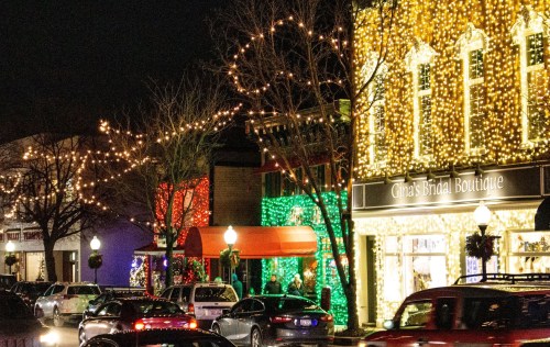 A festive street scene at night, adorned with colorful holiday lights on shops and trees.