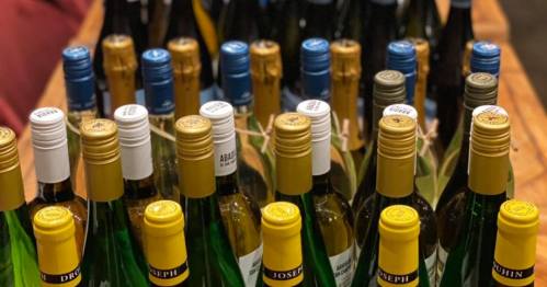 A close-up of various wine bottles with colorful caps arranged on a wooden table.