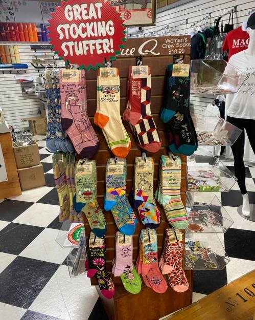 Display of colorful women's crew socks on a wooden stand, labeled "Great Stocking Stuffer!" in a retail store.