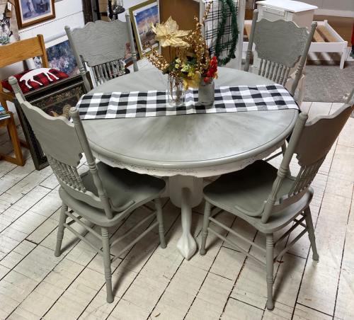 A round gray dining table with a checkered runner, surrounded by four matching chairs and a vase of flowers.