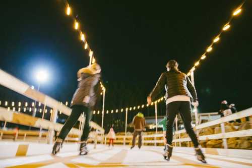 Two people ice skating at night, surrounded by string lights and a festive atmosphere.