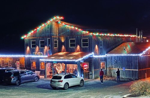 A festive building adorned with colorful lights at night, with people walking nearby and parked cars in the foreground.