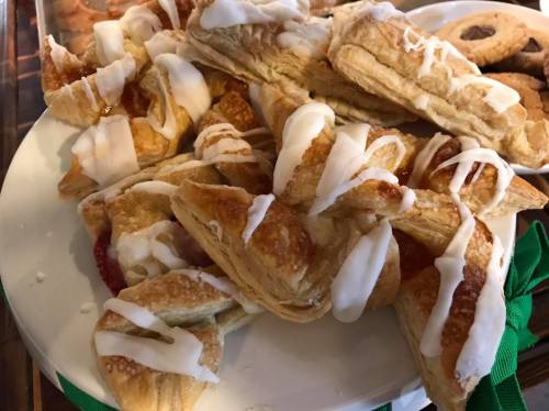 A plate of flaky pastries drizzled with white icing, alongside a variety of cookies.