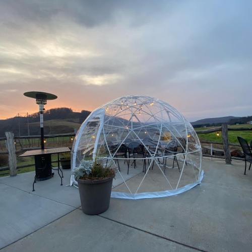 A clear dome structure with chairs inside, set against a scenic landscape at sunset.